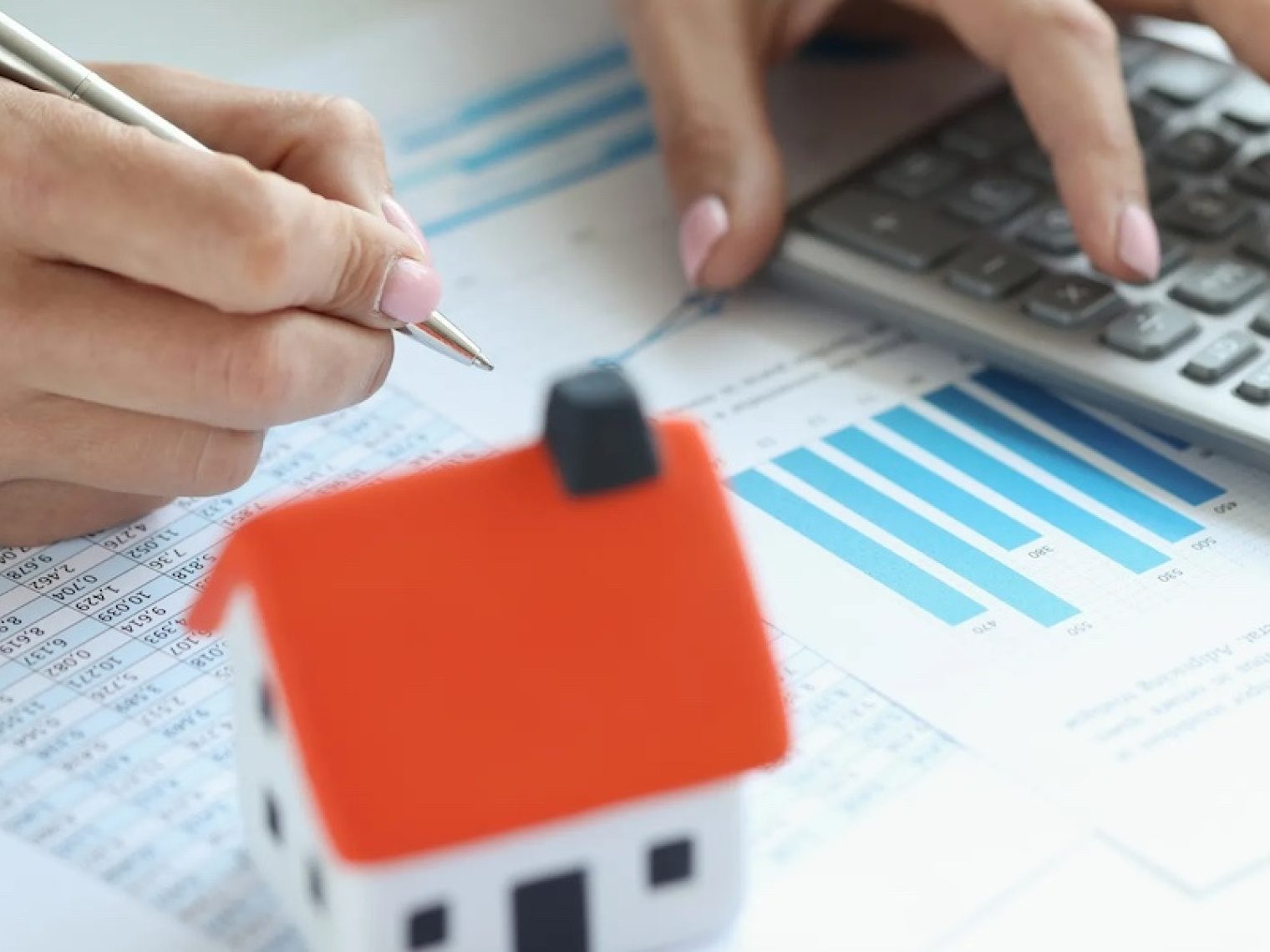 Person working with a calculator with a model of a home on the desk.