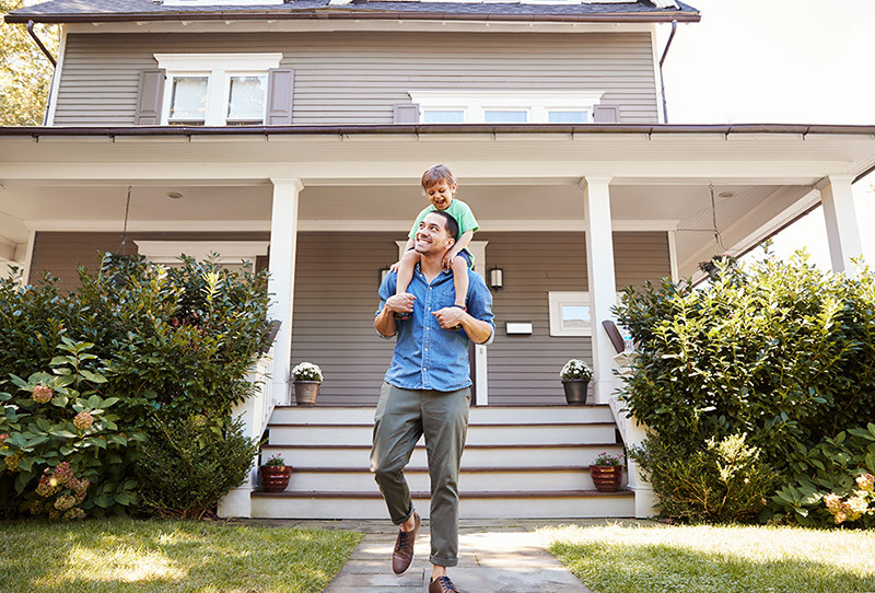 Father with his child on his shoulders outside their new home.